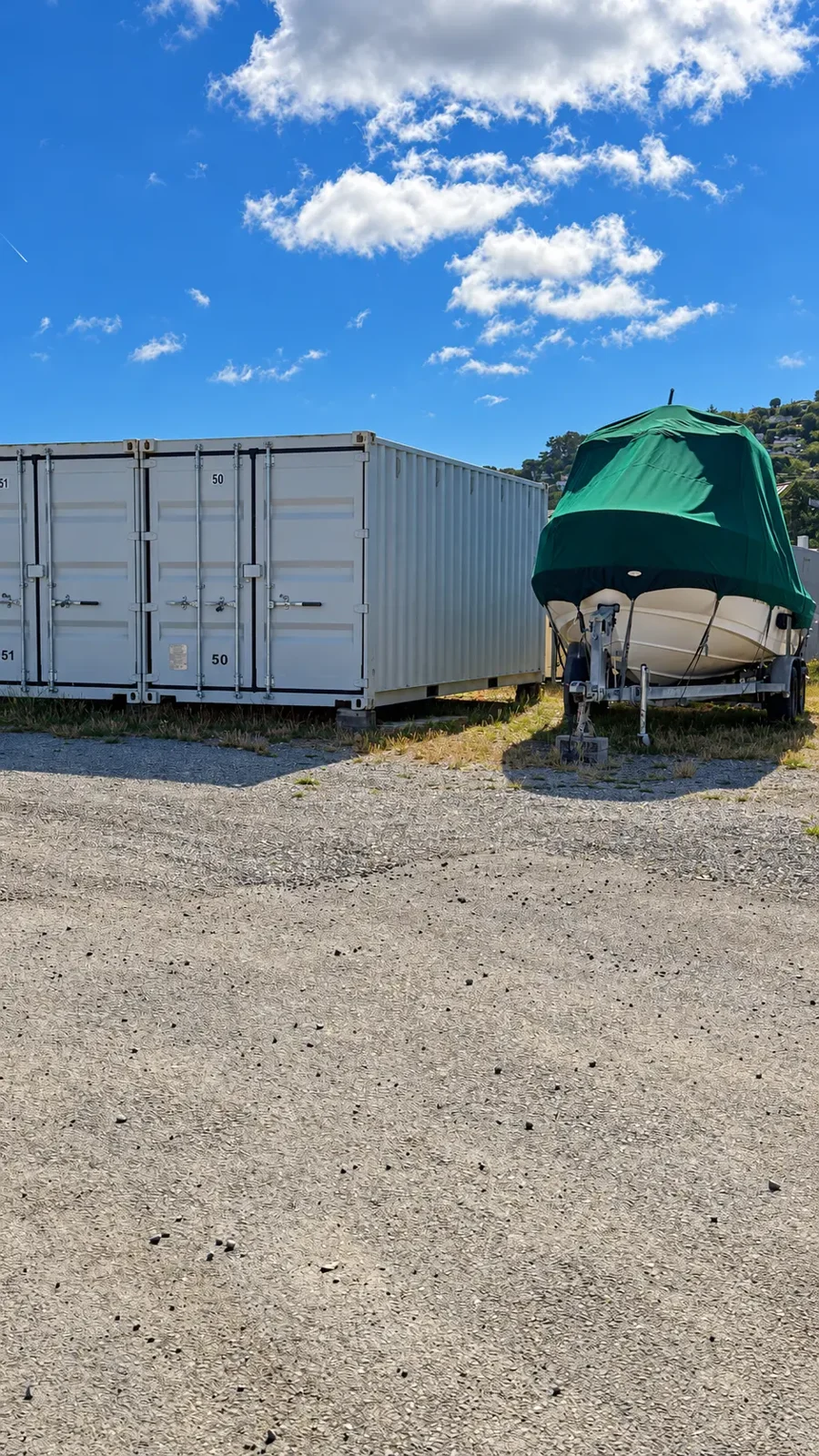 Green-covered boat on a trailer beside storage containers at Marinship Industries